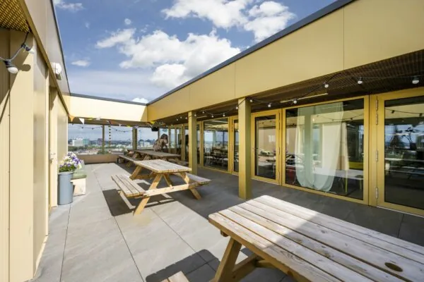 Zonnig dakterras aan de James Wattstraat met picknicktafels, gele gevels en uitzicht op de stad.